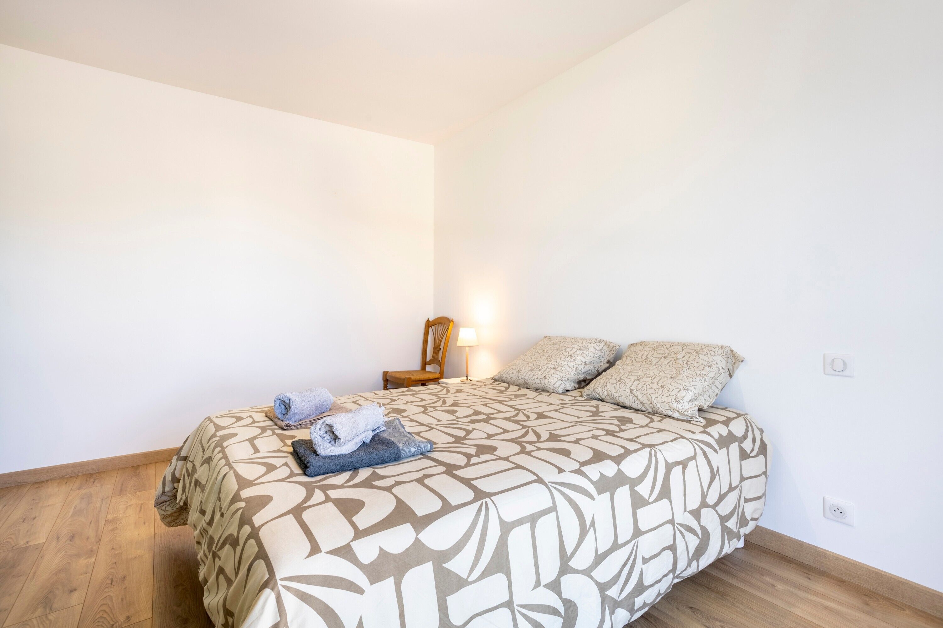 A bedroom with a bed, a chair, a lamp, and a wall socket.