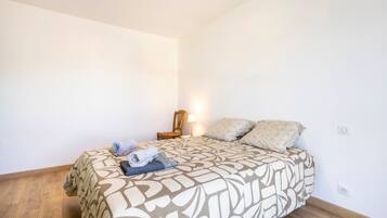 A bedroom with a bed, a chair, a lamp, and a wall socket.