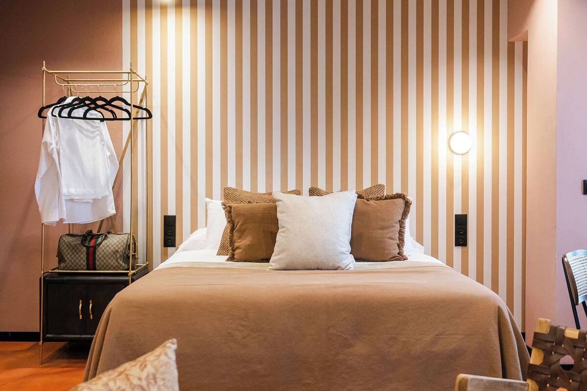 A modern hotel room with a large bed, a seating area, and a clothing rack.
