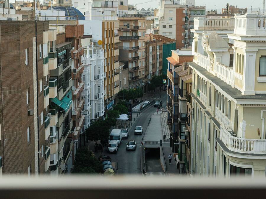 Rua urbana com edifícios em ambos os lados, céu claro e veículos na pista.