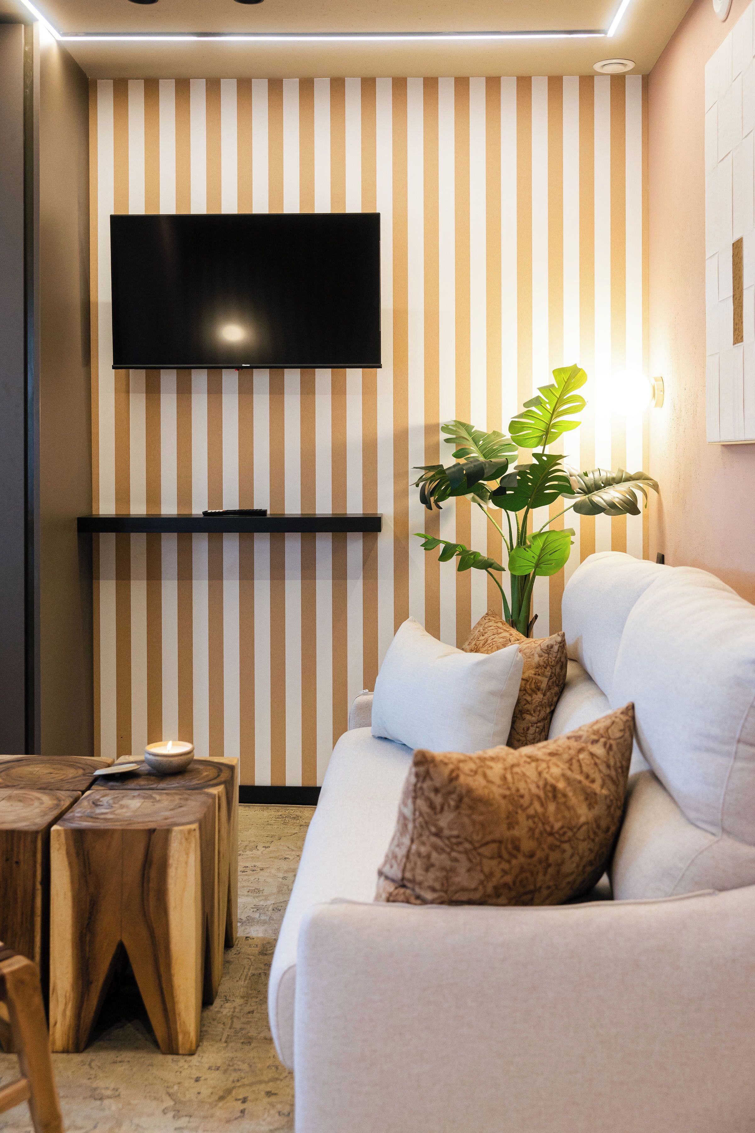 A modern living room with a sofa, a flat-screen TV mounted on the wall, a wooden coffee table, and a potted plant.
