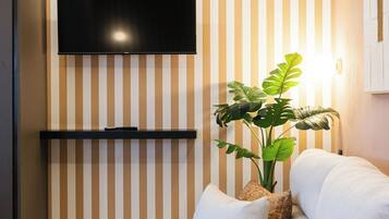 A modern living room with a sofa, a flat-screen TV mounted on the wall, a wooden coffee table, and a potted plant.