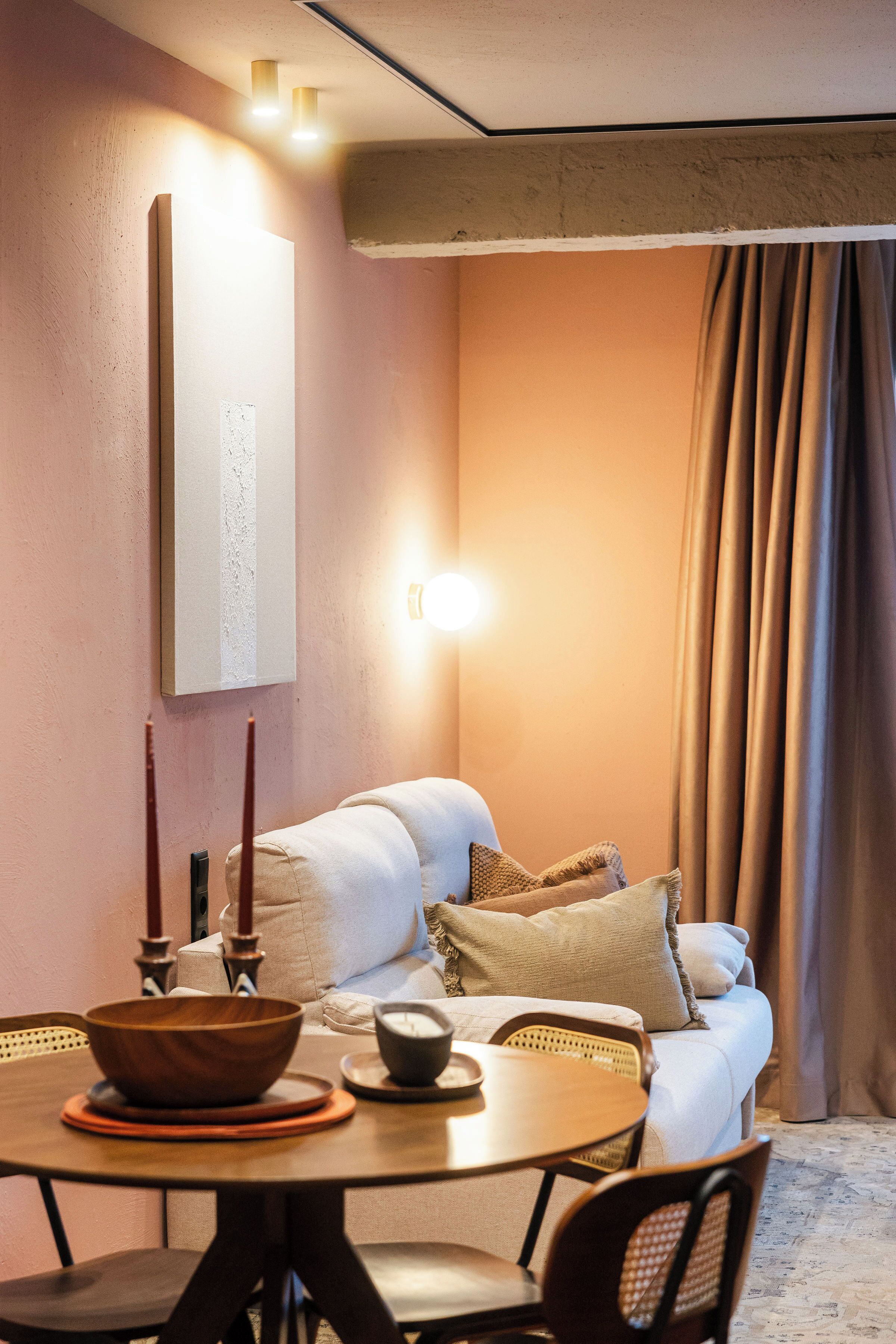 A cozy room with a sofa, a dining table with chairs, a wooden bowl, and a wall-mounted light fixture.