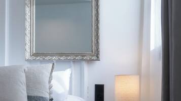 A neatly made bed with a white comforter and pillows, a bedside table with a lamp, and a large mirror on the wall.