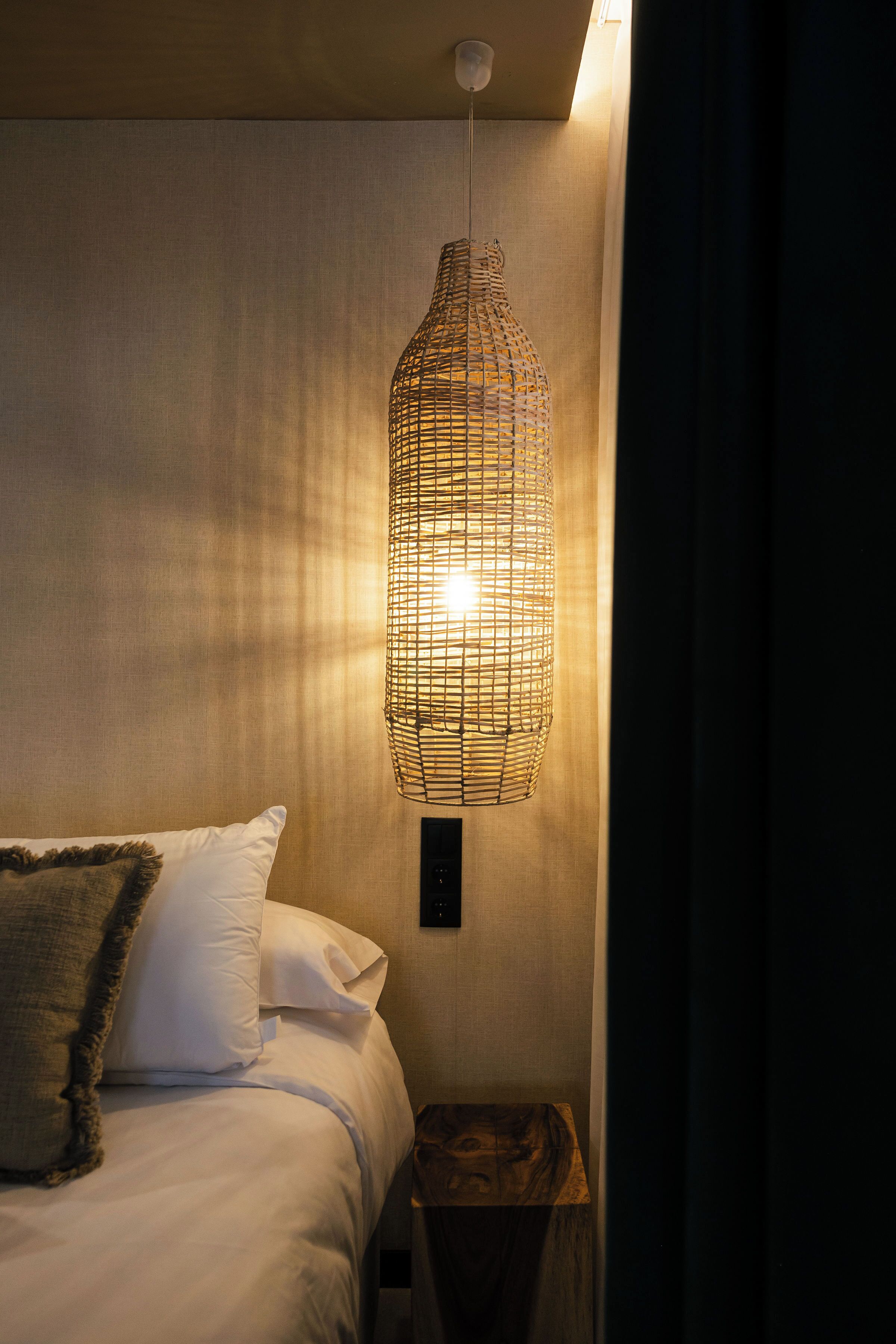 Un lit avec du linge de lit blanc, un coussin décoratif à motifs et une petite table de chevet en bois avec une lampe.