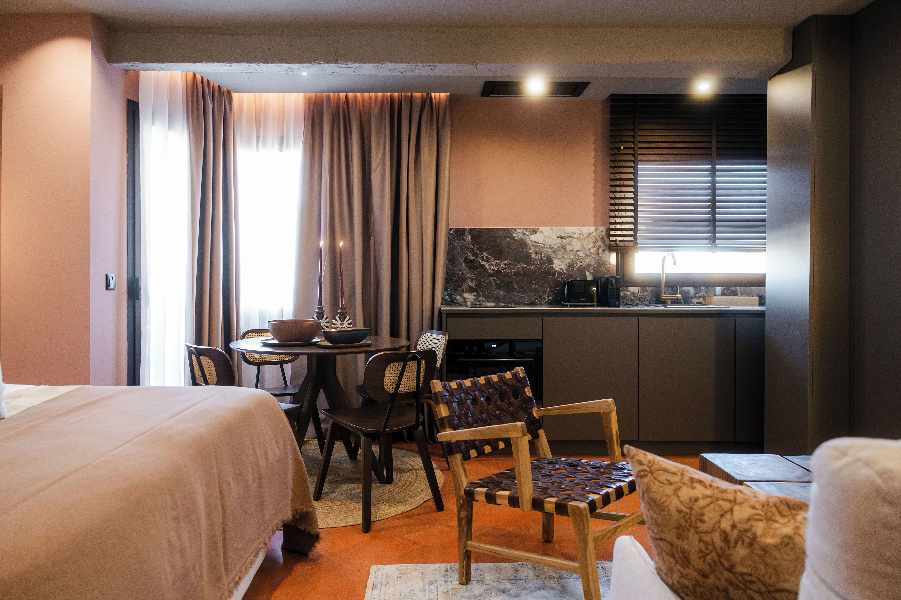 Habitación de hotel compacta con cama, mesa de comedor con sillas, zona de cocina y ventana con cortinas.