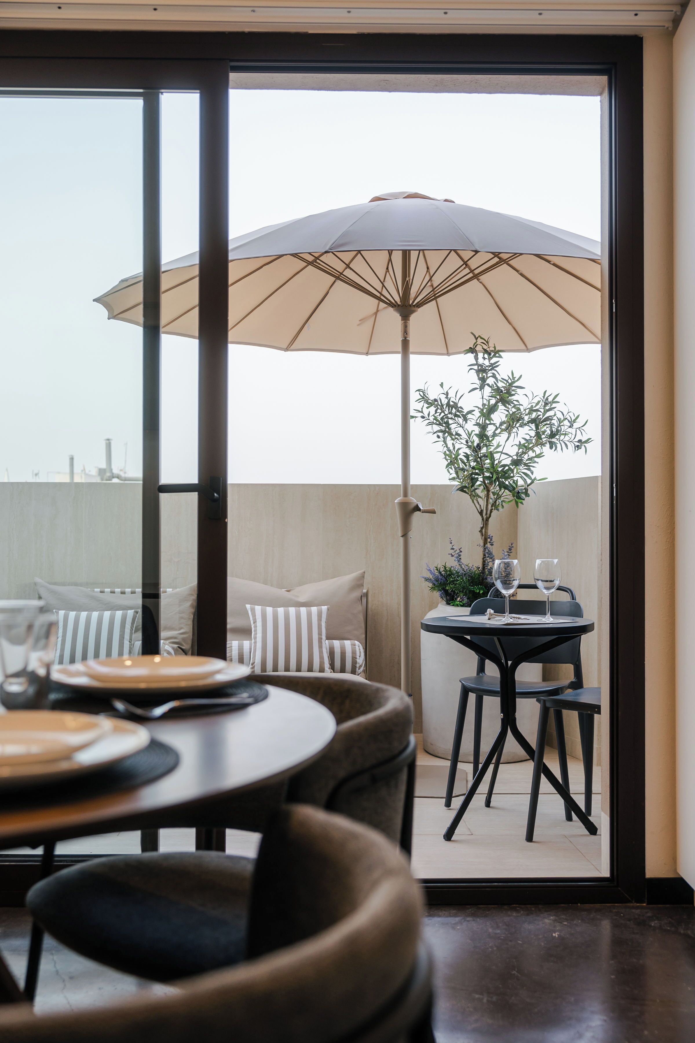 A dining area with a table, chairs, and an umbrella. There is a view of a building in the background.