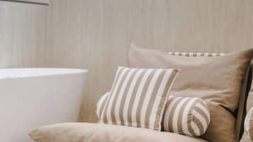 Una habitación moderna y minimalista con un sofá beige y almohadones a rayas, una mesita de noche blanca y una pared de madera clara.