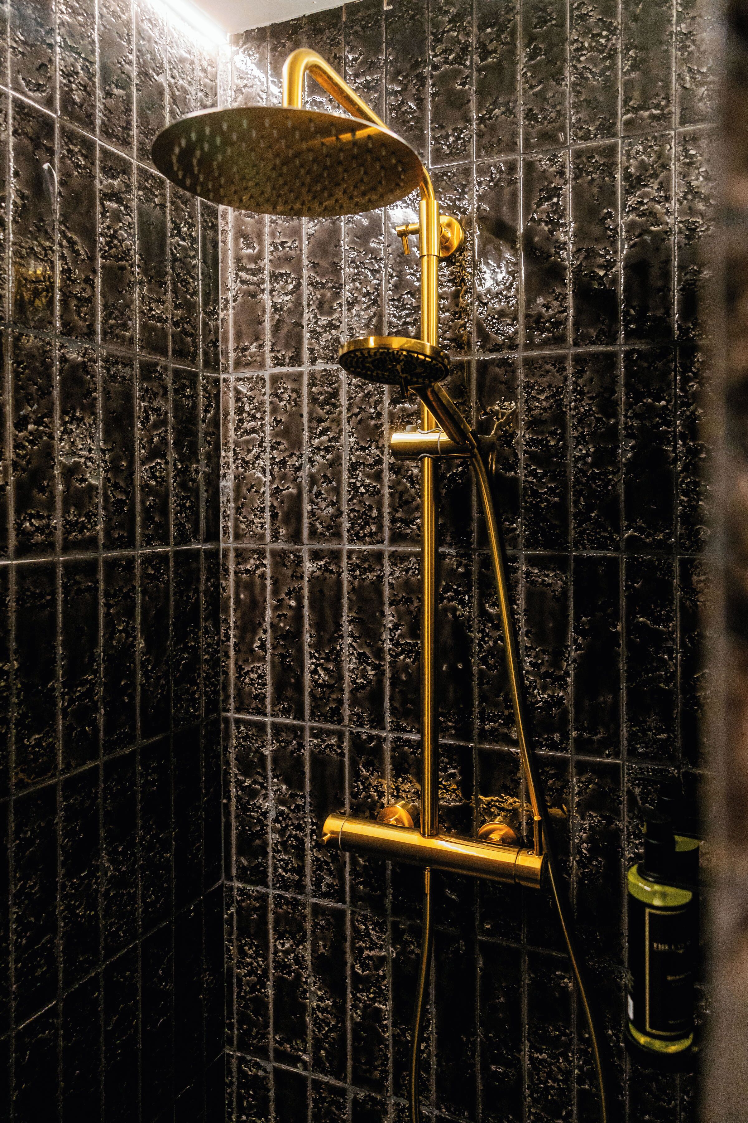 A shower with a golden fixture against a tiled wall.