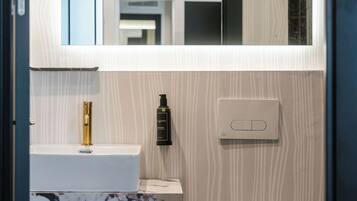 Ein Badezimmer mit Toilette in Weiß, Marmorwaschbecken, Goldarmatur, einer schwarzen Flasche und einem Lichtschalter.