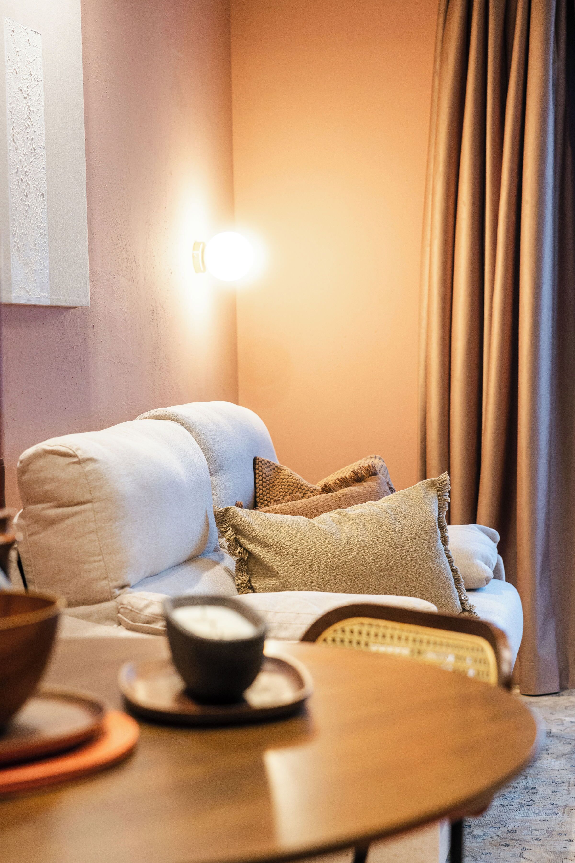 A cozy room with a sofa, a small table with a cup and saucer, and a wall-mounted light.