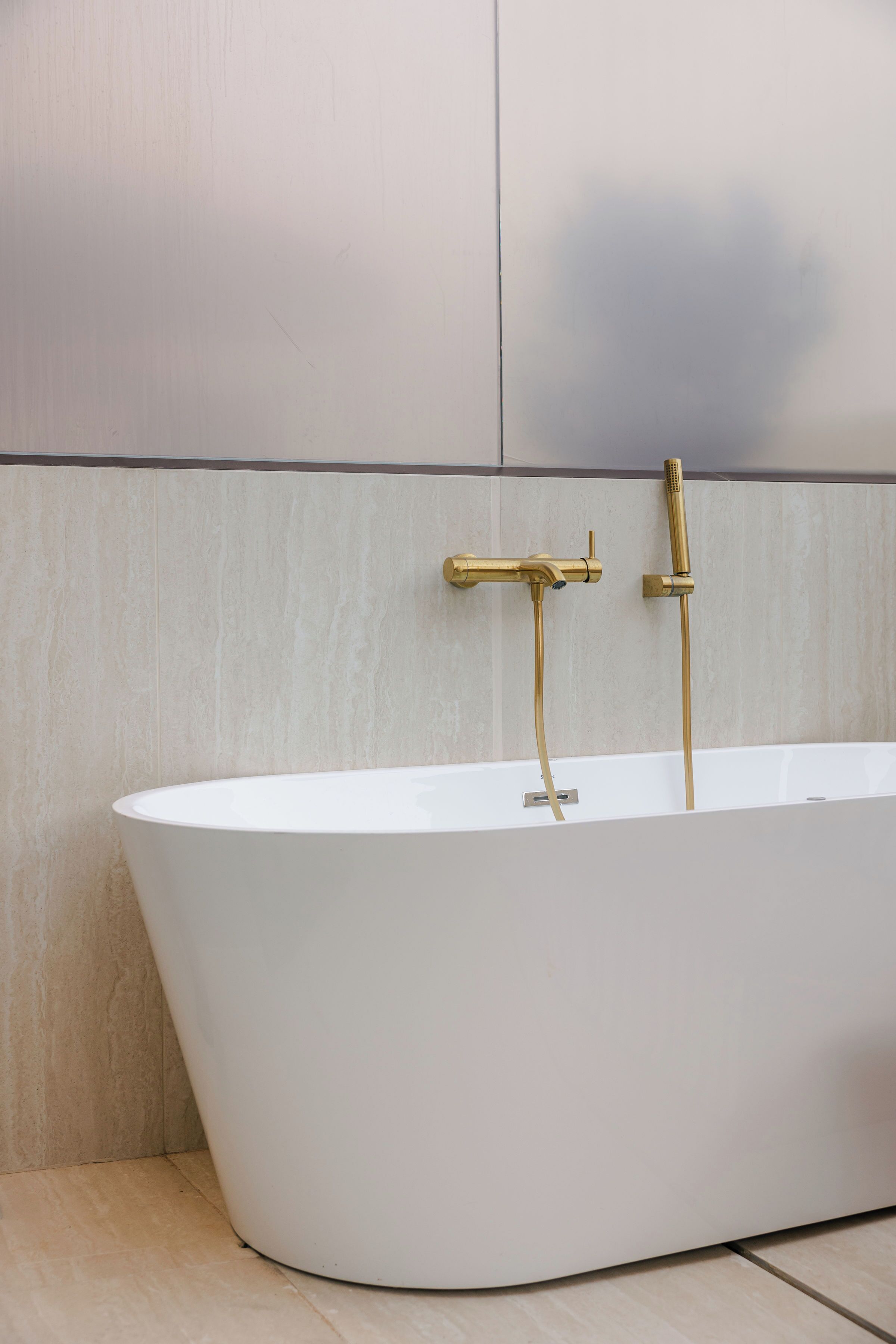 Une baignoire sur pied, dotée de robinetterie dorée, placée devant un mur carrelé.