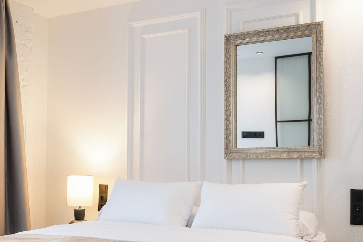 A neatly made bed with white linens, a bedside lamp, and a mirror on the wall.