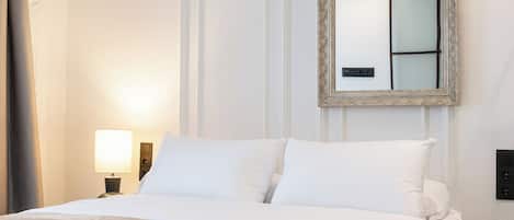 A neatly made bed with white linens, a bedside lamp, and a mirror on the wall.