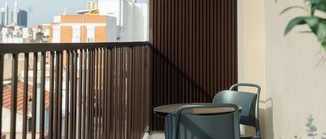 A balcony with a view of the cityscape, featuring a wooden railing, two chairs, and a small table.