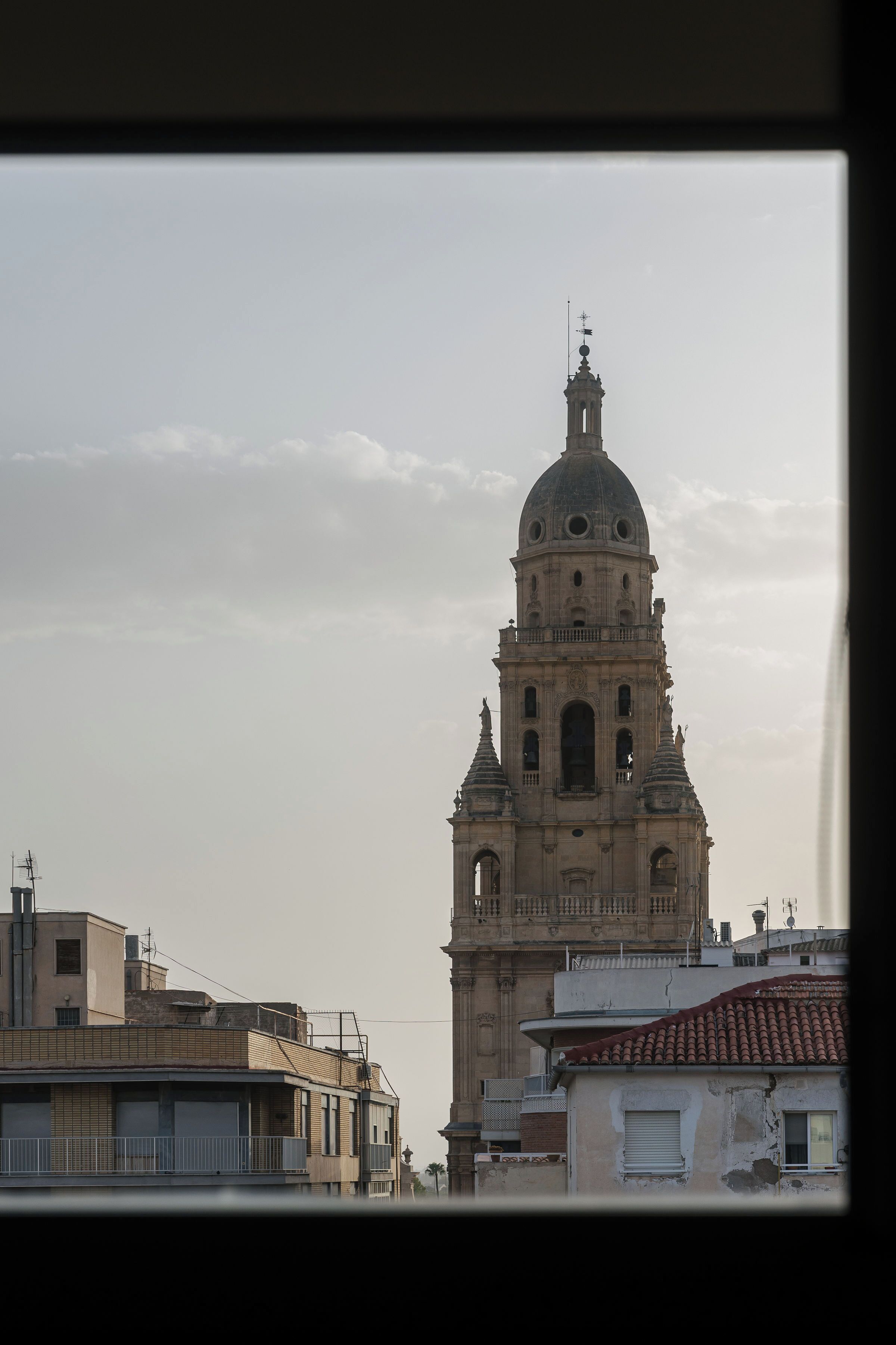 A historic building with a prominent dome and bell tower, viewed from a window overlooking a cityscape.