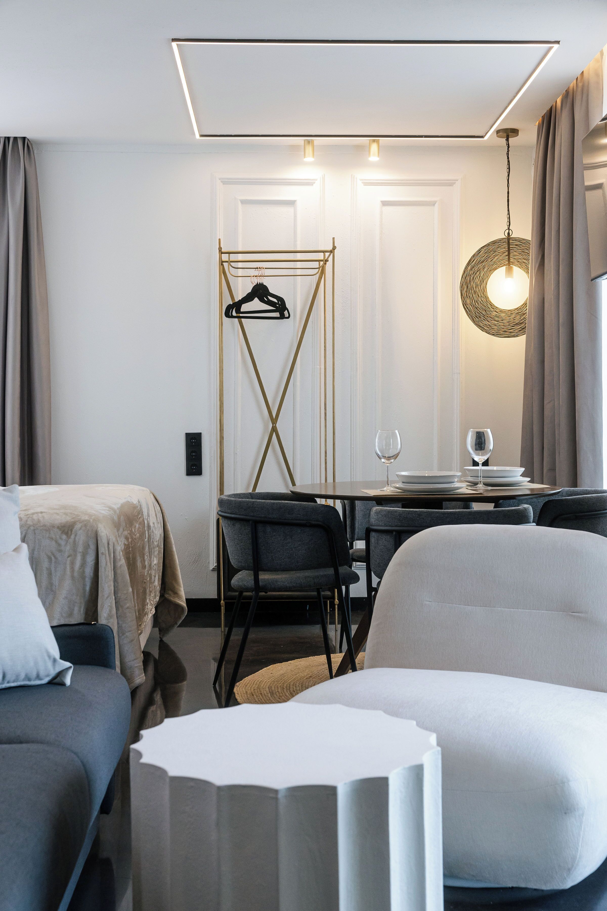 A hotel room with a bed, a desk with a chair, a dining table set for two, and a hanging light fixture.