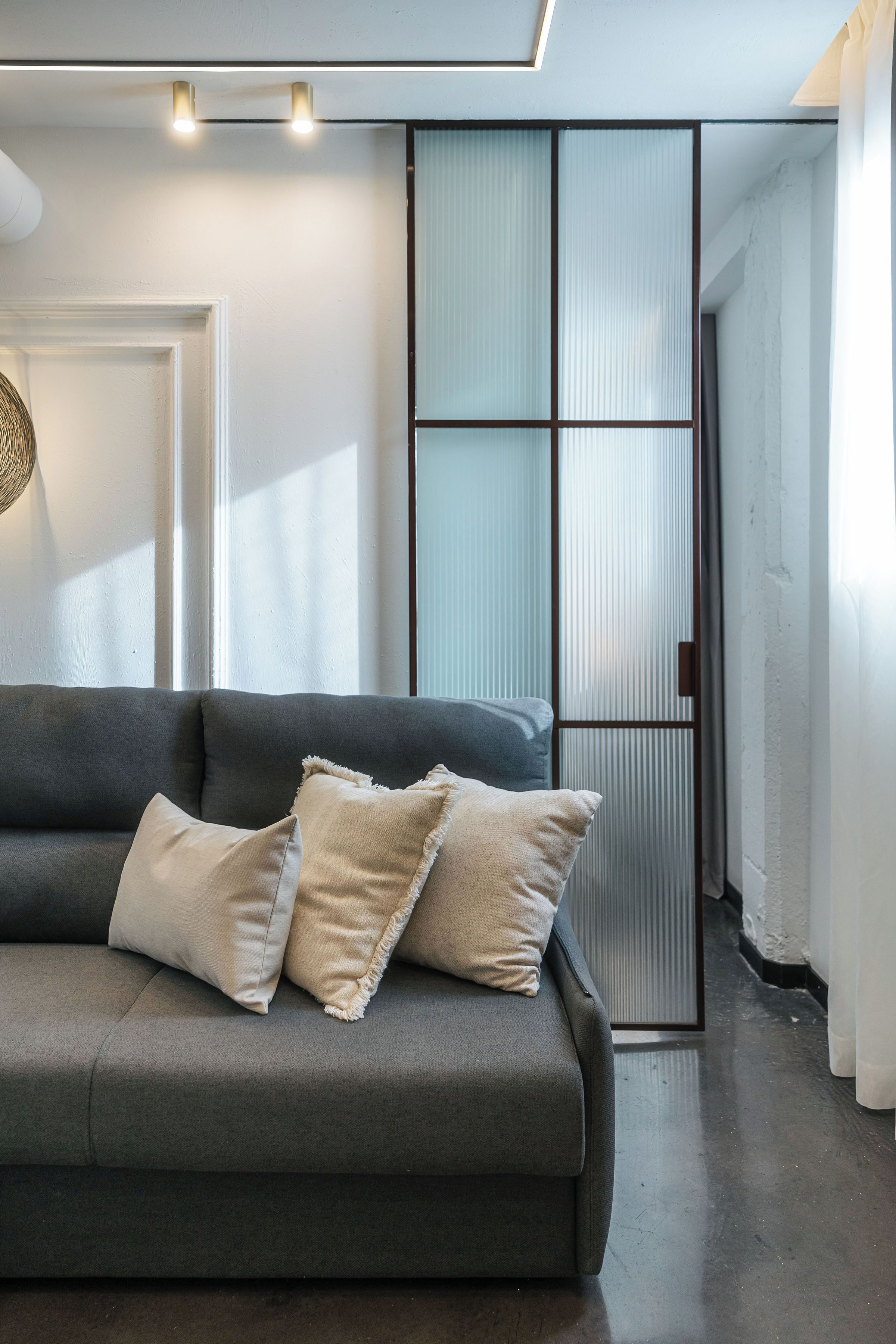 A modern living room with a grey sofa, two beige pillows, and a woven wall hanging.