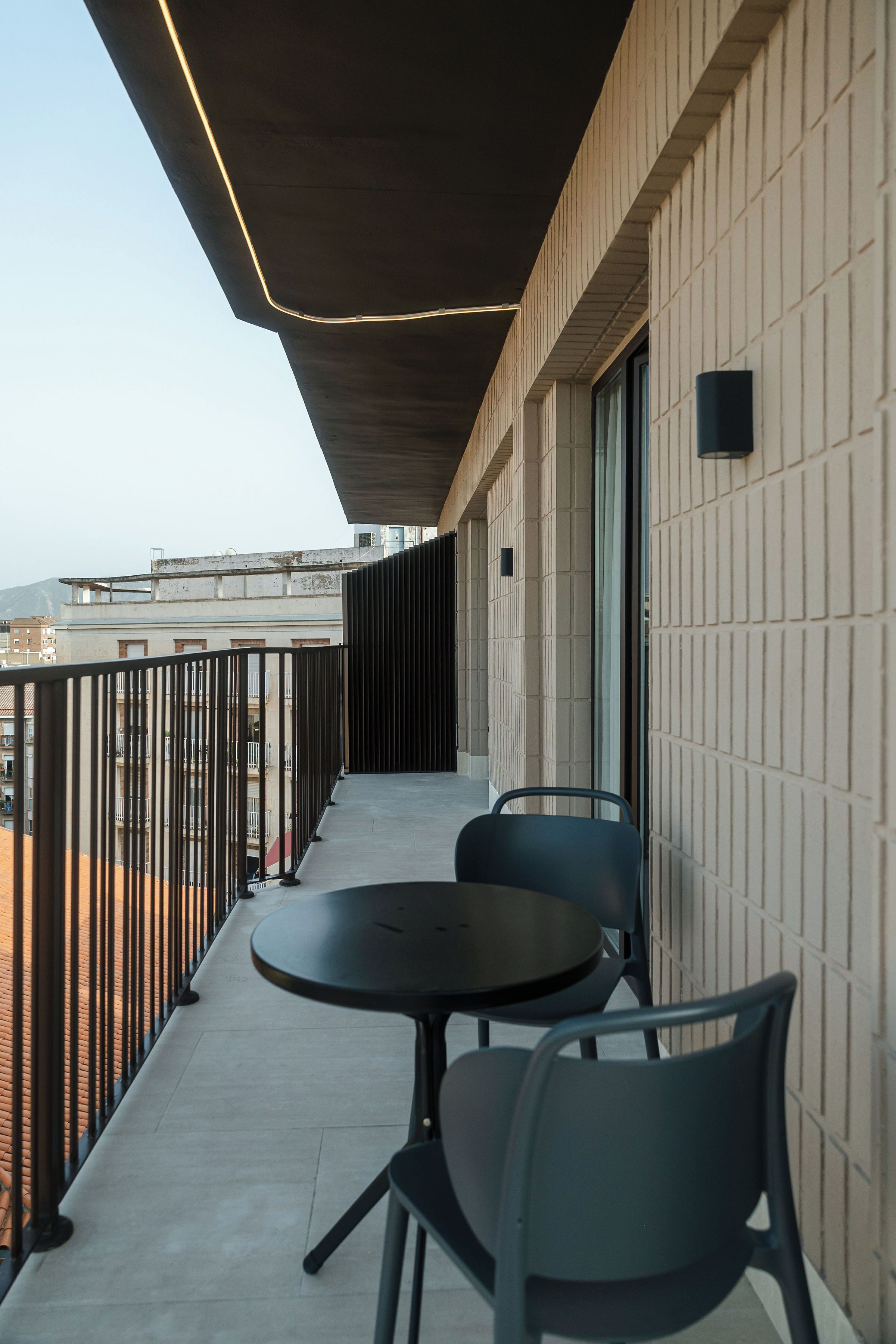 A balcony with two chairs and a table, a tiled floor, and a view of buildings in the background.