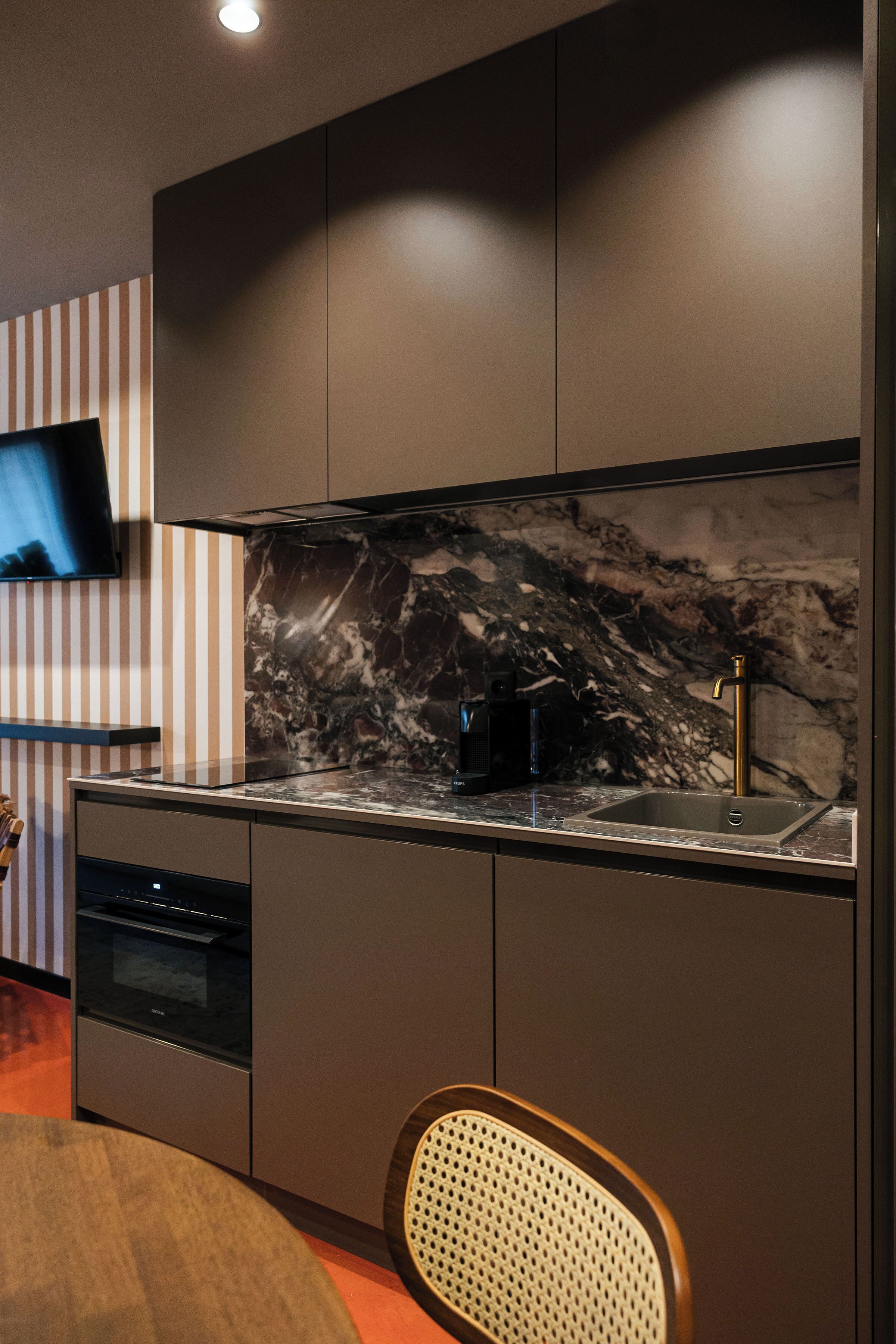 Una cocina moderna con salpicadero de mármol, horno empotrado y televisor de pantalla plana en la pared.