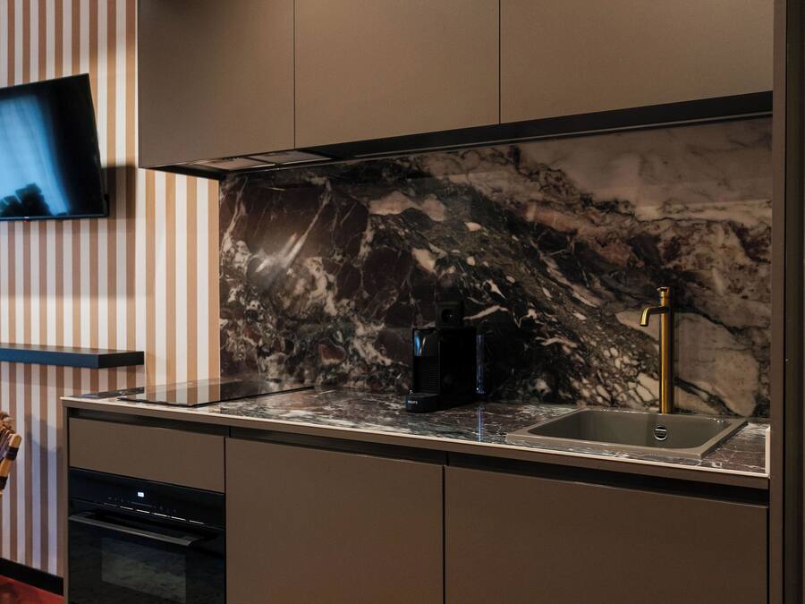 Eine moderne Küche mit Marmor-Spritzschutz, einem Einbauofen und einem flachbildfernseher an der Wand.