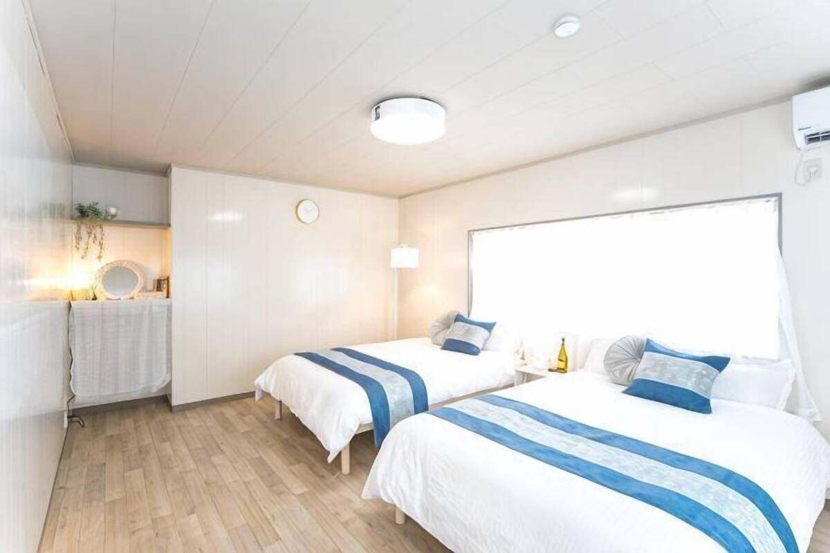 Ein Hotelzimmer mit zwei Betten, einem kleinen Tisch, einer Lampe und einem Fenster.