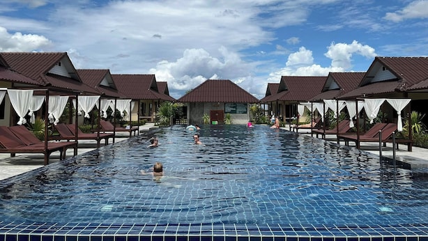 A swimming pool with lounge chairs and umbrellas, surrounded by buildings with brown roofs.