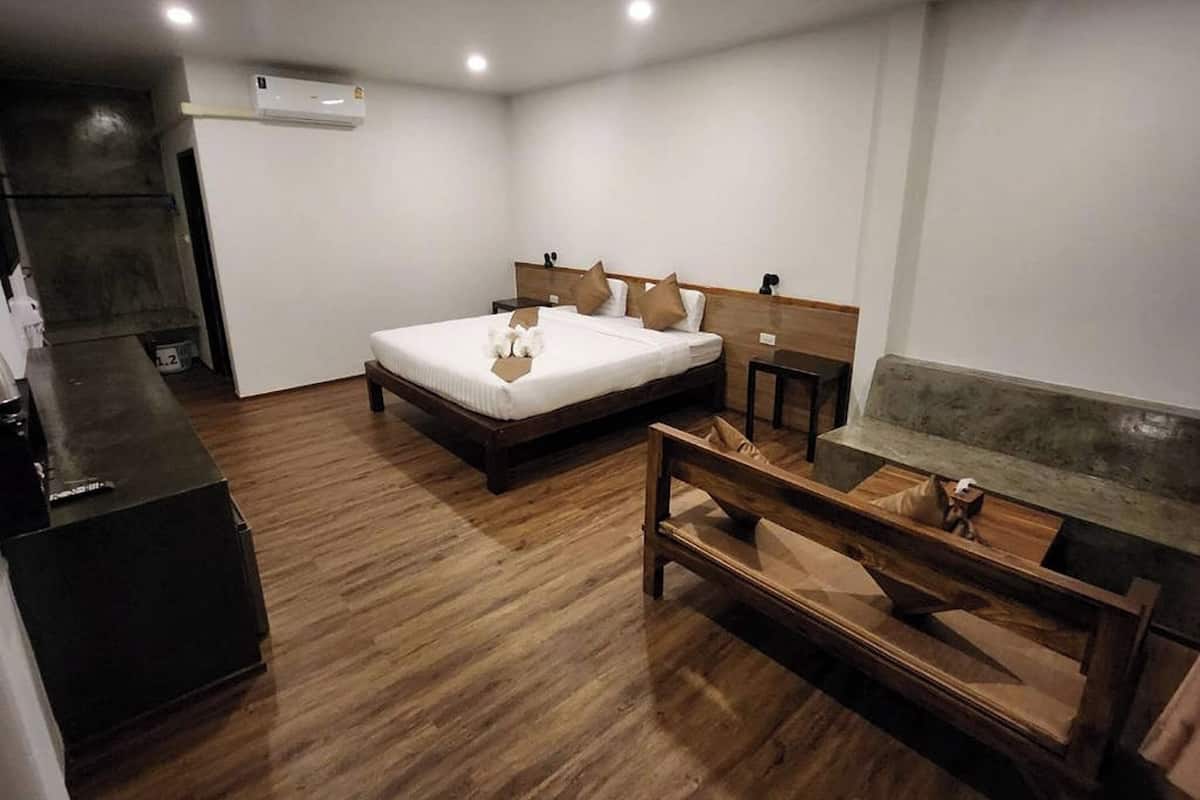 Habitación de hotel con una cama de madera, un banco, una mesita pequeña y un equipo de aire acondicionado.