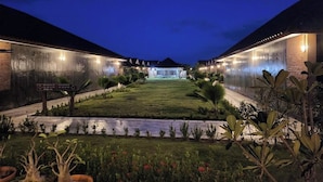 A hotel courtyard at dusk with a well-maintained lawn, potted plants, and a sign indicating amenities.