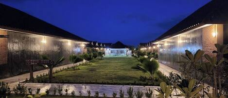 A hotel courtyard at dusk with a well-maintained lawn, potted plants, and a sign indicating amenities.