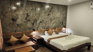 A hotel room with a large bed, a smaller bed, a wooden bench, and a nightstand with a lamp.