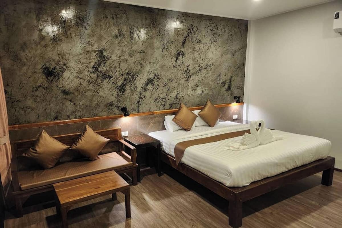 Habitación de hotel con una cama grande, una cama más pequeña, un banco de madera y una mesita de noche con lámpara.