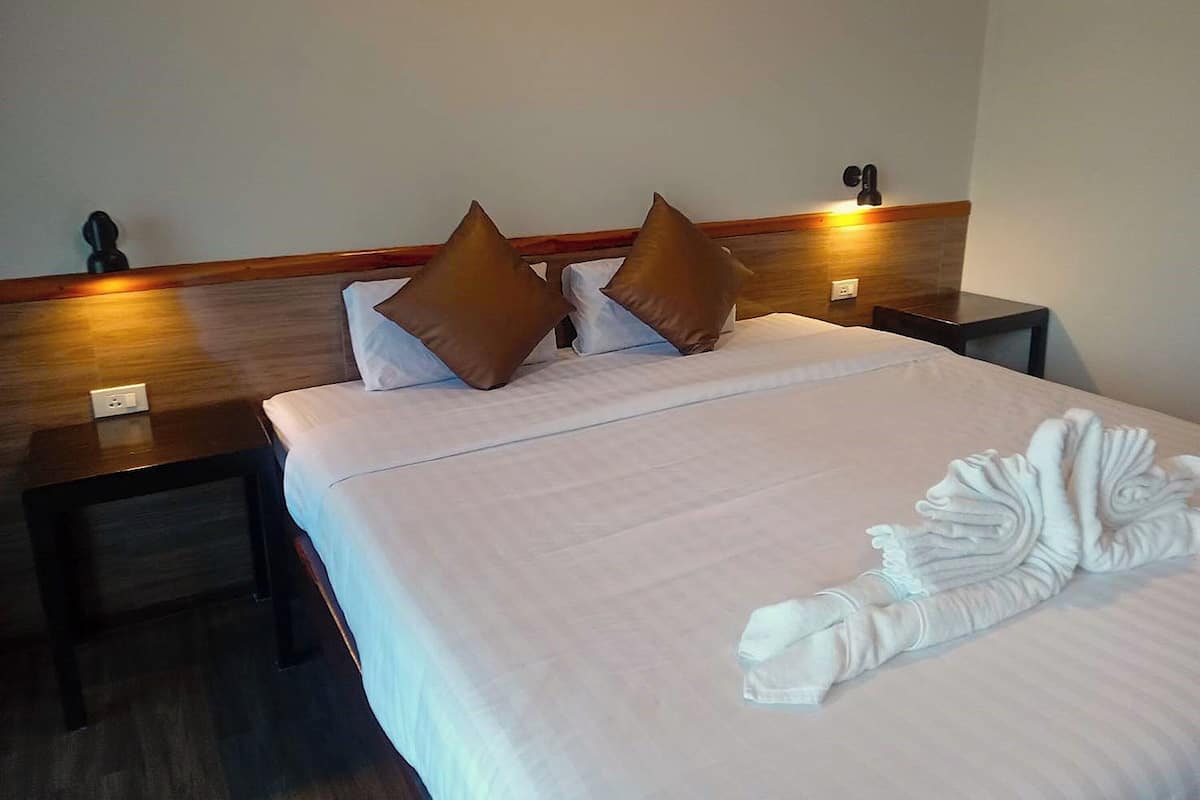 Habitación de hotel con una cama bien hecha, dos almohadas marrones, cabecera de madera, mesitas de noche y un aplique de pared.
