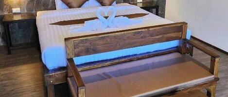 A bed with a heart-shaped decoration on the pillows, a wooden bench, and a remote control on the bench.
