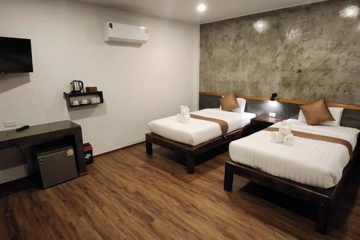 A hotel room with two beds, a TV, a shelf with toiletries, and a small desk.
