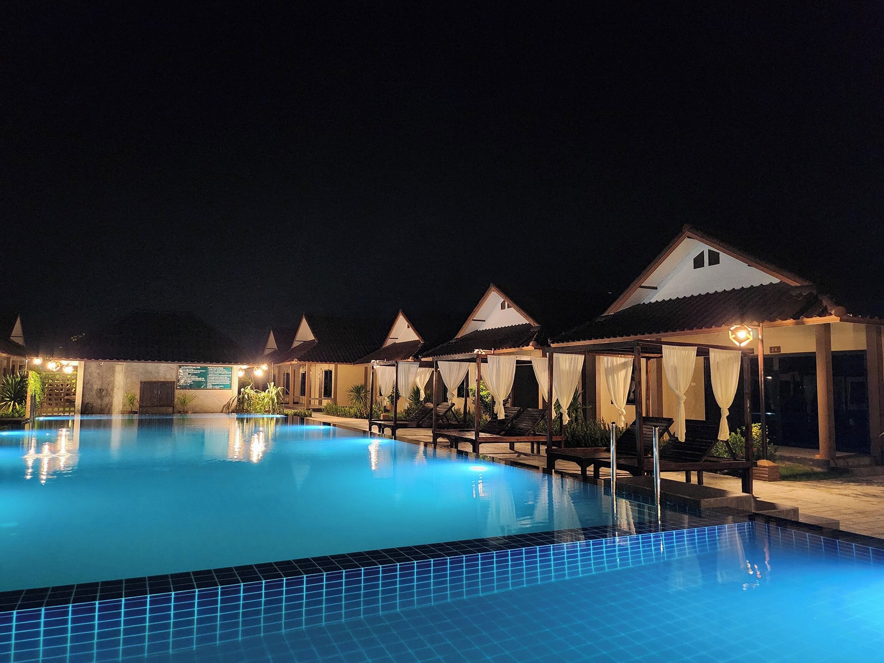 A nighttime swimming pool area with multiple overwater bungalows.