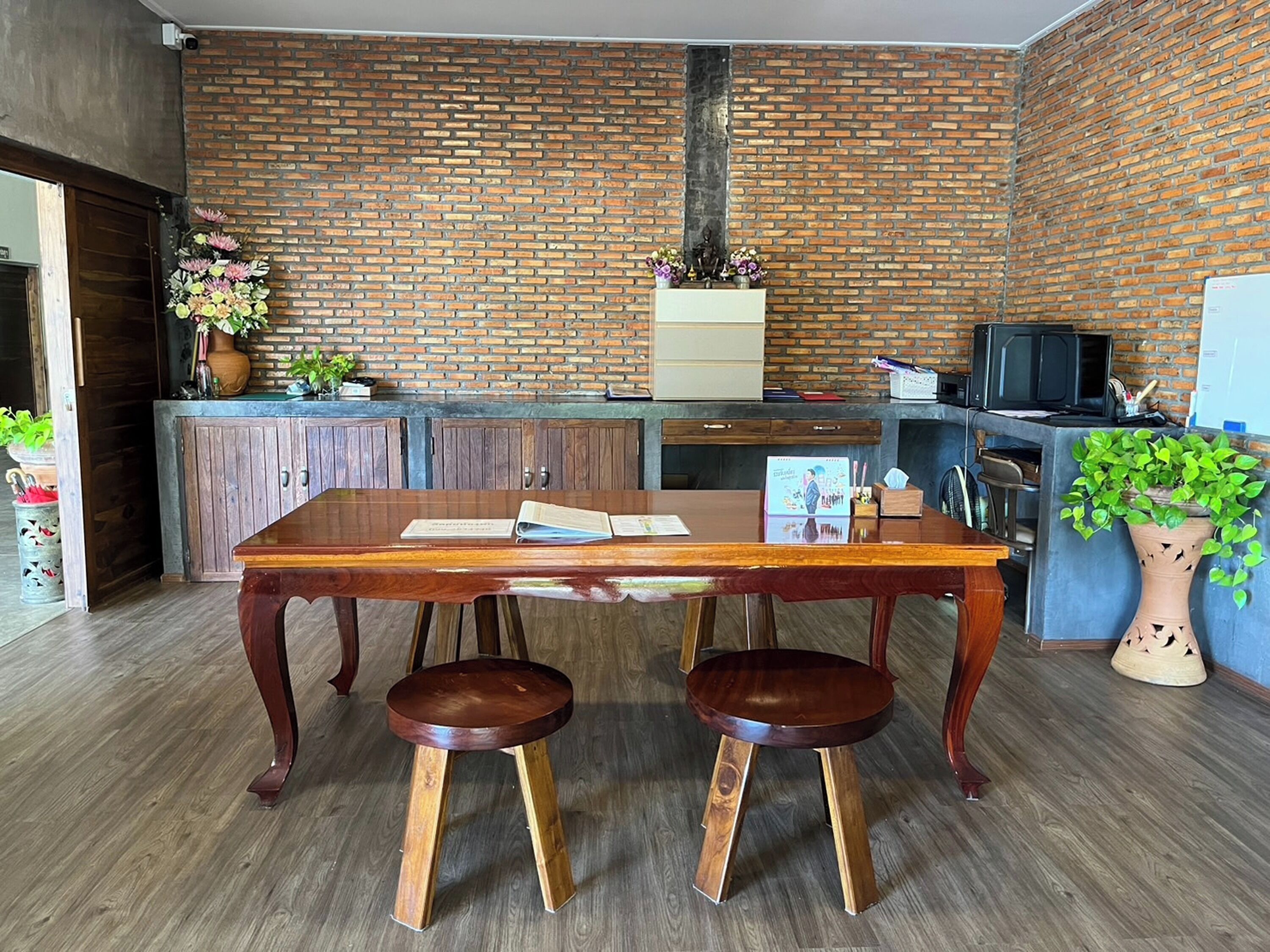 Een keuken met een bakstenen muur, houten kastjes, een houten eettafel met twee krukken en een potplant.