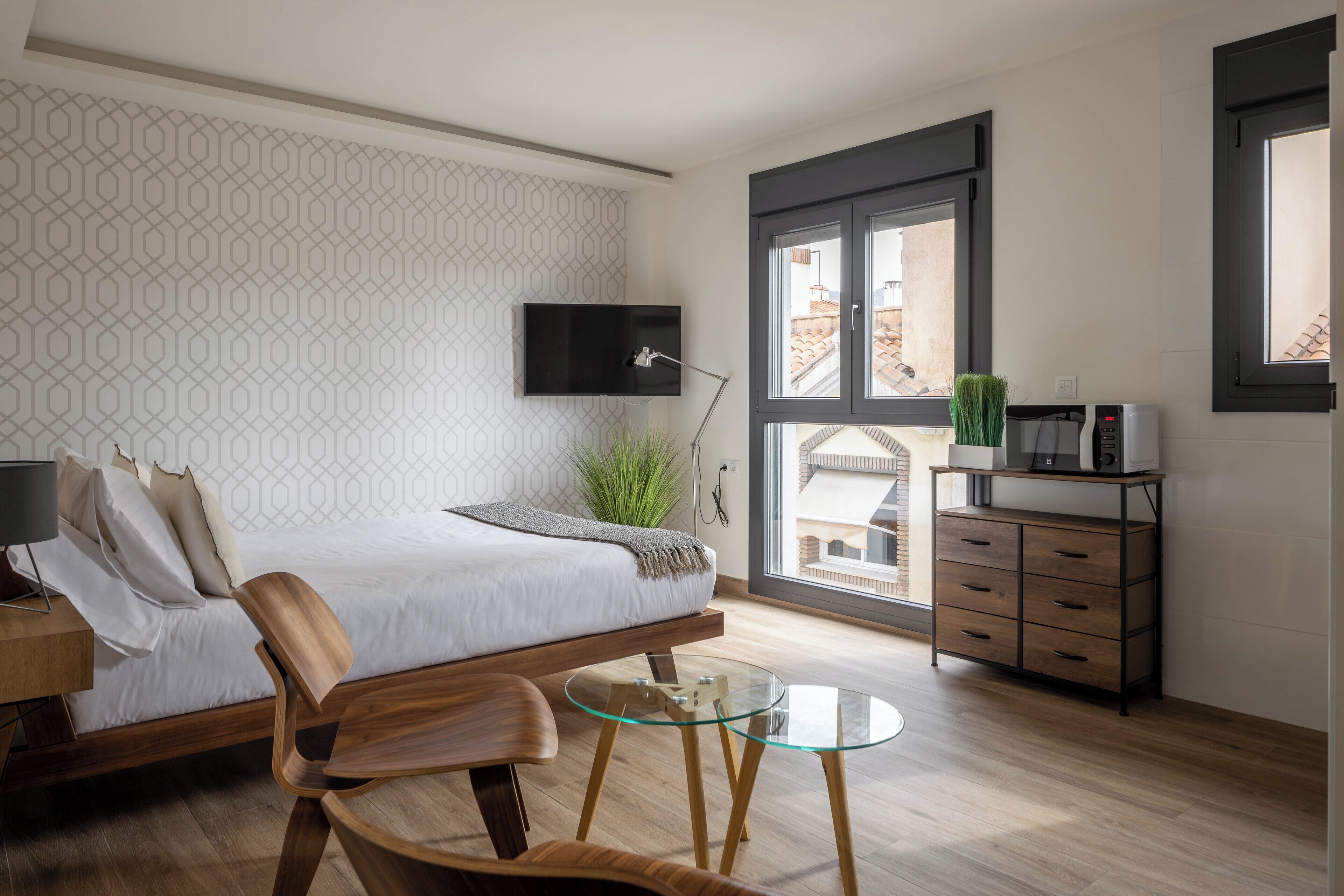 Een moderne slaapkamer met een bed, een aan de muur bevestigde televisie, een houten dressoir en een glazen tafel.