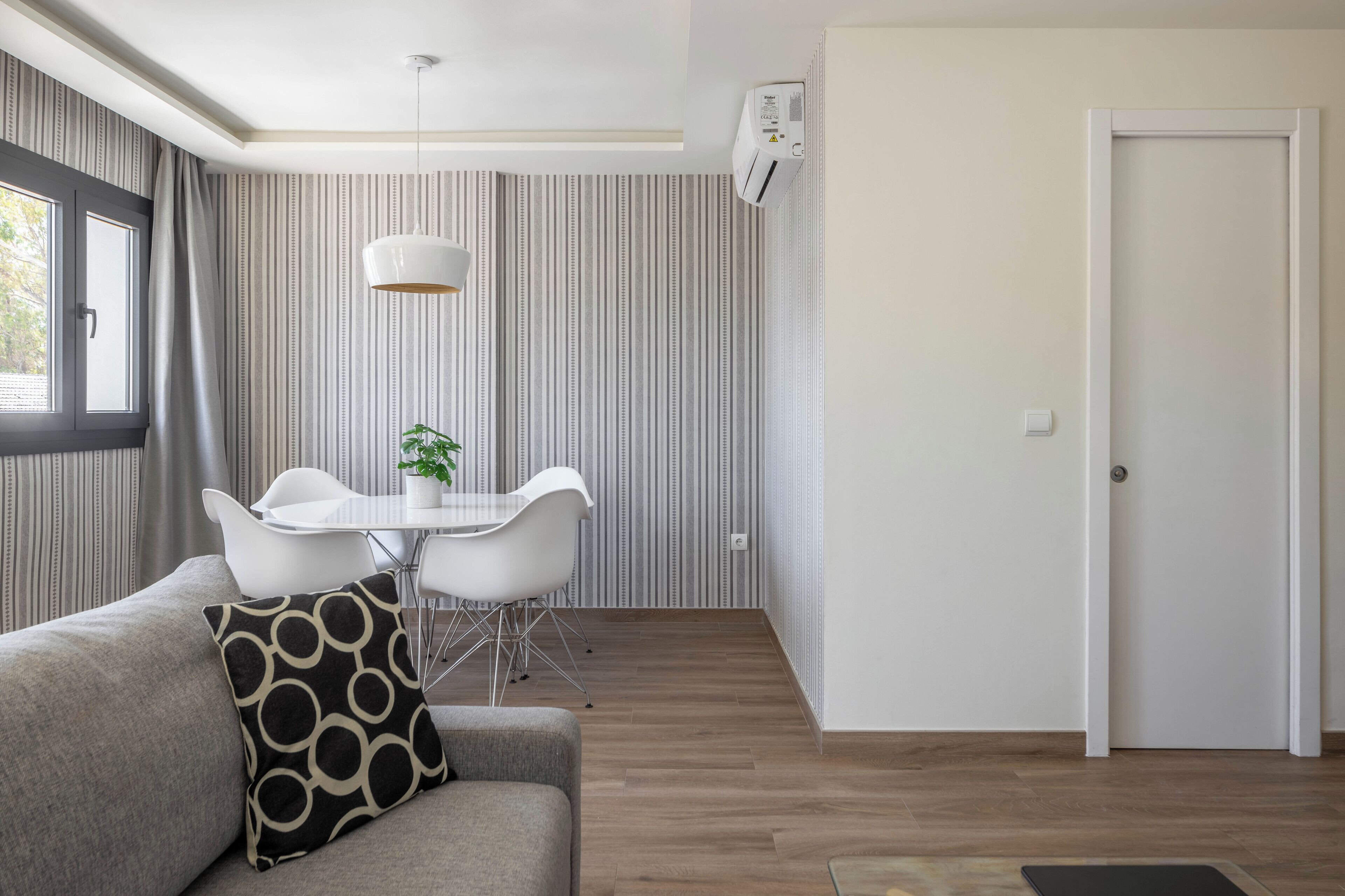 A modern living room with a grey sofa, a dining table with white chairs, and a hanging pendant light.