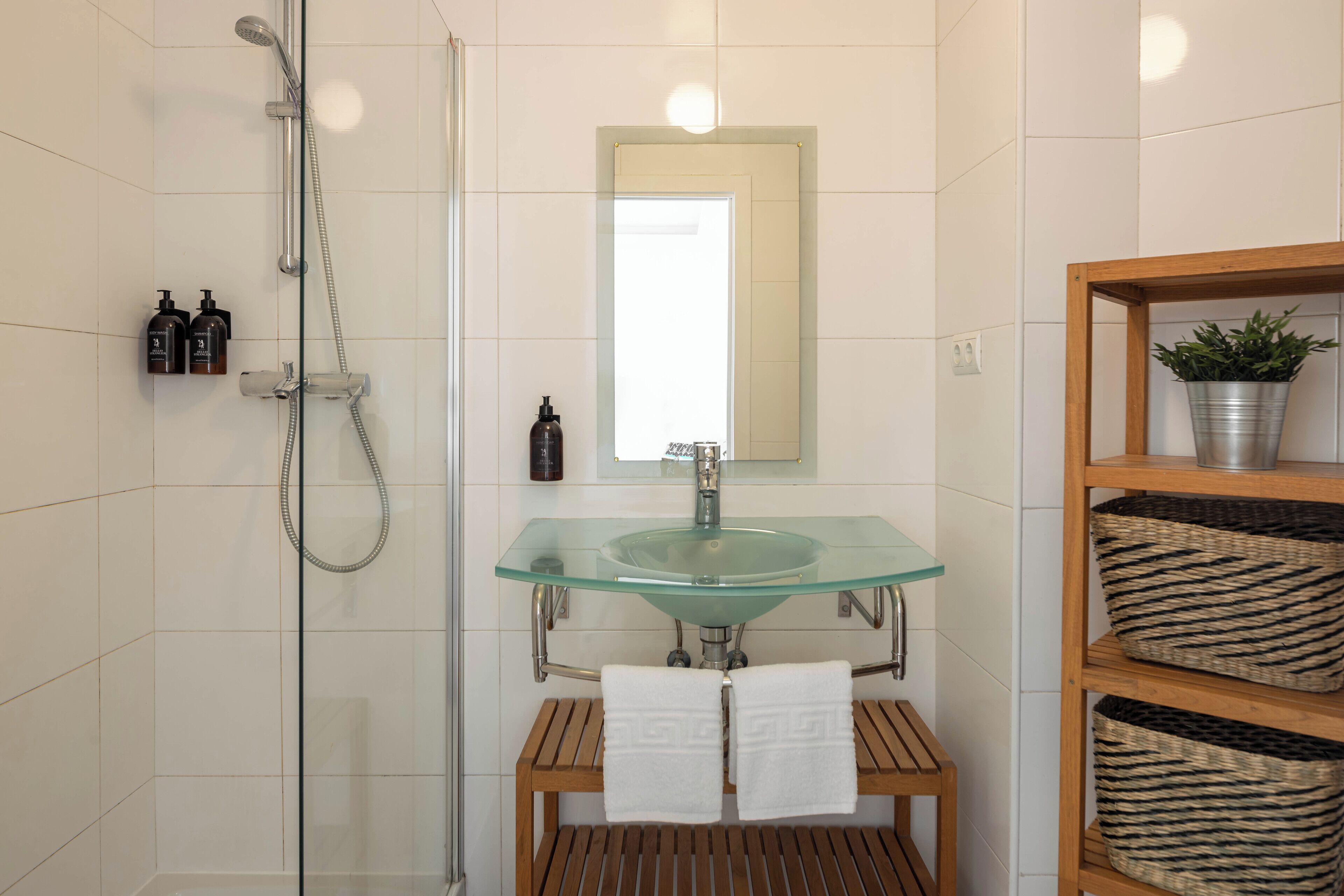 Un baño moderno con lavamanos de vidrio, tocador de madera, ducha con puerta de vidrio y un espejo sobre el lavamanos.
