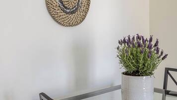 Un coin repas avec une table ronde, quatre éléments décoratifs en fibres tressées accrochés au mur et une plante en pot ornée de fleurs violettes.