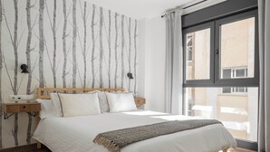 Un dormitorio con una cama grande, cabecera de madera, mesita de noche con lámpara y ventana con cortinas.