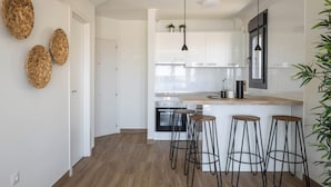 Una cocina moderna con armarios blancos, una isla central con taburetes e iluminación colgante.