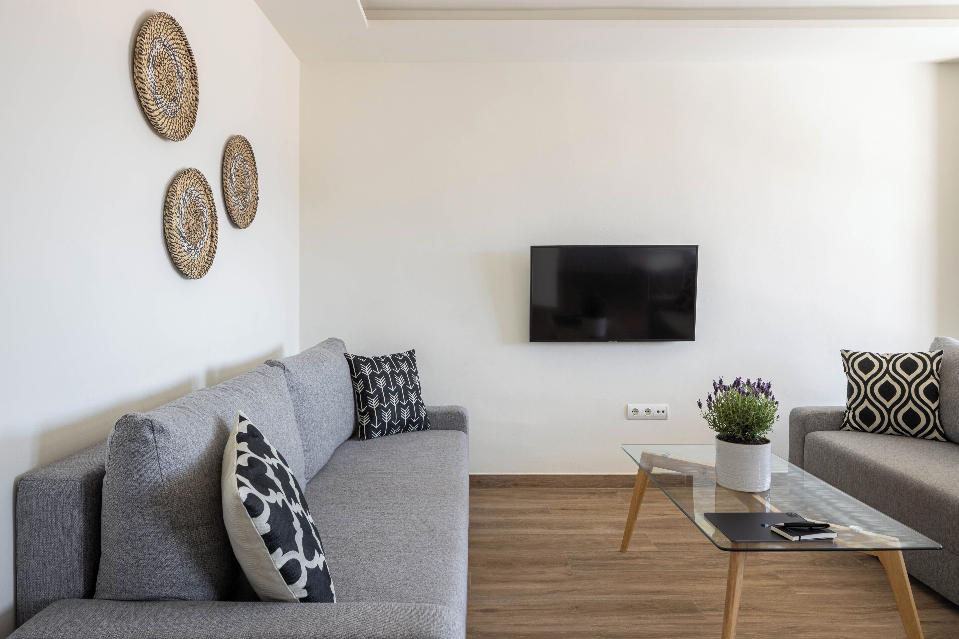 Una sala de estar moderna con un sofá gris, una mesa de centro de vidrio y decoración en la pared.