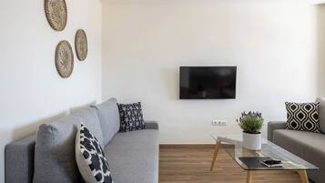 Una sala de estar moderna con un sofá gris, una mesa de centro de vidrio y decoración en la pared.