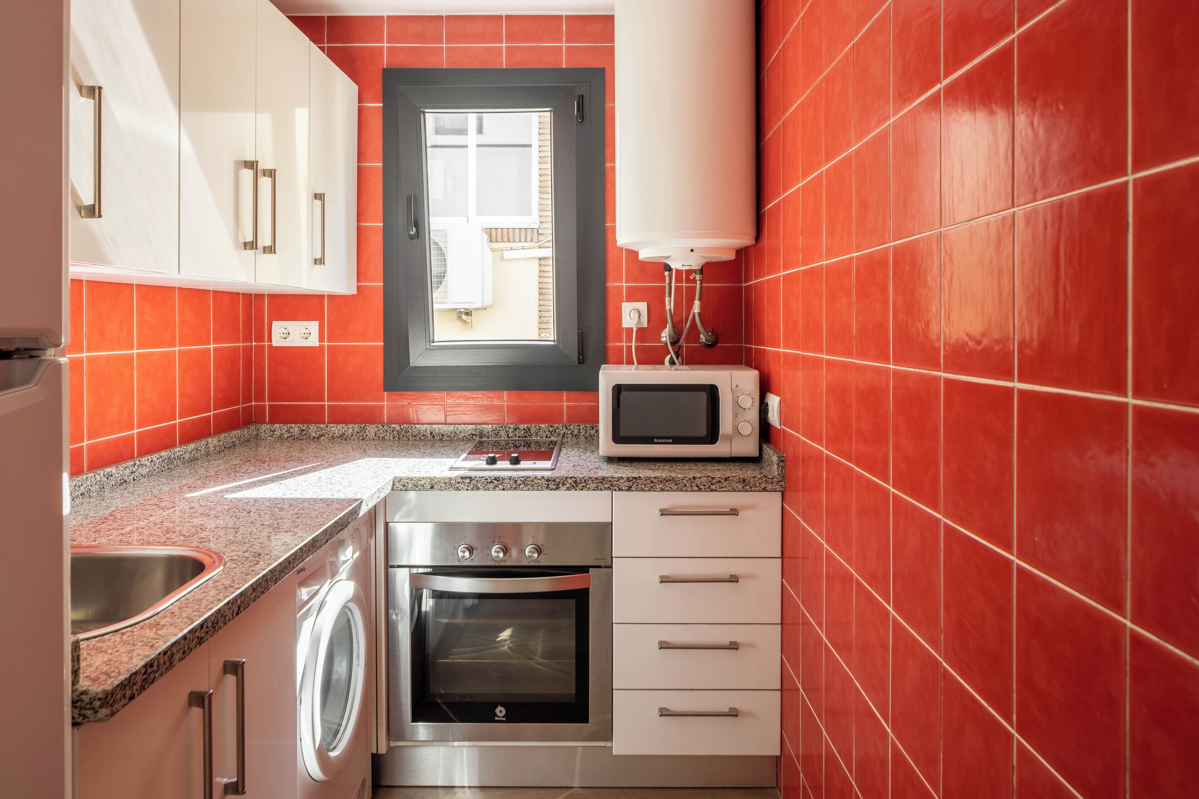 Cocina compacta con lavadora, horno, microondas y ventana con vistas.