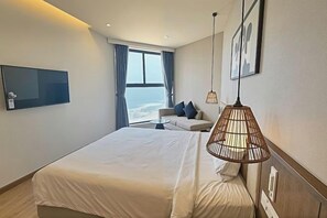 A hotel room with a large bed, a sofa, a TV, and a window with a view.