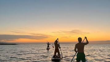 Three people paddleboarding on a calm body of water during sunset.