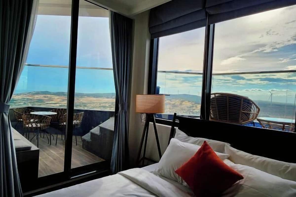 Une chambre d’hôtel avec un grand lit, une vue sur le paysage, un balcon avec des chaises et une lampe.