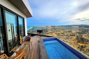 Una piscina infinita en la azotea con vistas a un paisaje desértico, una parrilla y sillas de mimbre.